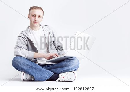Portrait of Serious Handosme Blond Caucasian Man Sitting with Laptopp on Legs. Posing Against White Background. Horizontal Image Composition