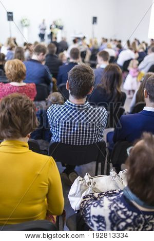 Group of People Sitting in hall During a Conference. Two Male Hosts Speaking on Stage in Front of the Audience.Vertical Shot