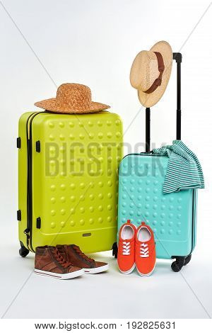 Suitcases, hats, clothes, shoes. Strawy hat on large luggage. Man and woman summer clothes.
