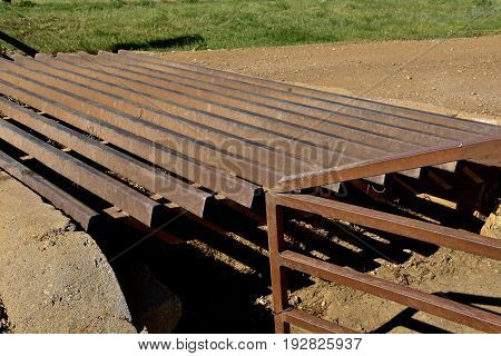 A  closeup of a metal grated cattle guard crossing a gravel road
