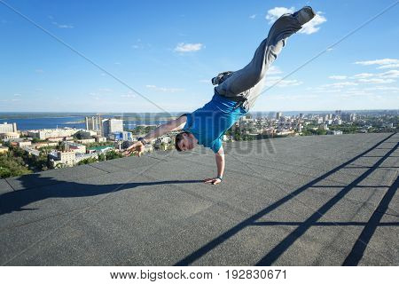 Roofer stands on his hands on the edge of the roof. Extreme acrobatics. Courage and adrenaline. Parkour and Roofing.