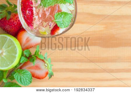 Top view strawberry lemon lime mojito in clear glass on rustic wood table. Infused water: strawberry soda made with strawberry lemon or lime and mint leaf with copy space for background or wallpaper. Strawberry soda on white plank.