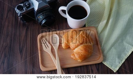 Cup of black coffee  with croissant,   camera, wooden table, travel concept