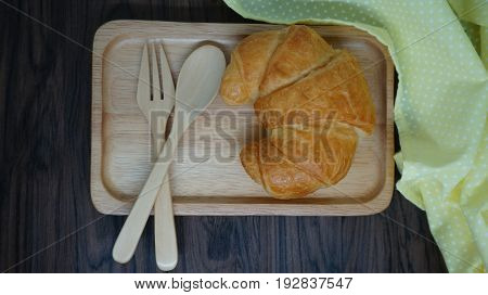 Croissant  on wooden plate with spoon and fork and coffee cup  on table