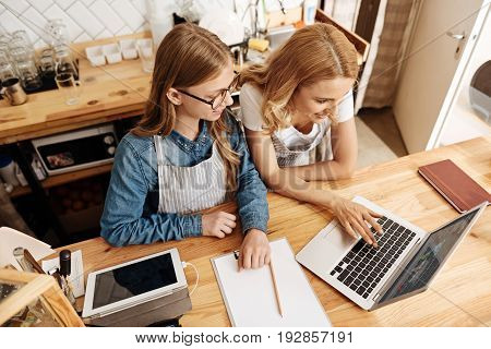 Fruitful collaboration. Close-knit mother and daughter standing behind a counter of their own cafe and creating new concept ideas for their business