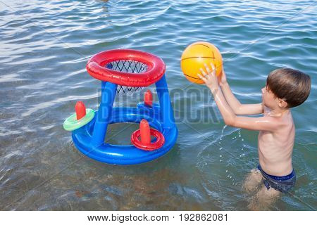 A boy on the beach playing in the water with an inflatable ball. Little boy playing basketball in the water. Boy beach water game ball.