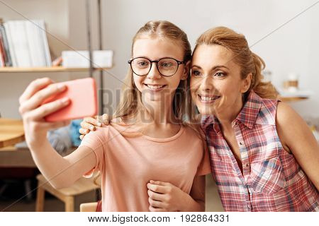 Joyful faces. Beautiful single-parent family, consisting of mother and daughter, sitting in a coffee bar and taking a selfie together
