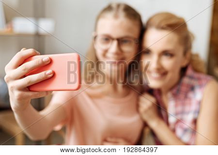 Neat and delicate. The focus being on a dainty hand of a teenage girl holding a phone in a coral case while taking a selfie with her dear mother