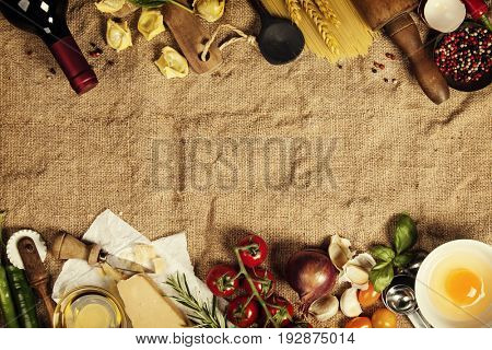 Italian food background with vine tomatoes, basil, spaghetti, spinach, onion, parmesan, olive oil, garlic, peppercorns, rosemary and eggs. Burlap background