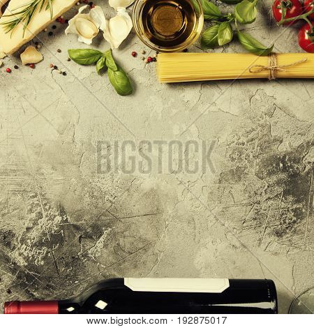 Italian food background with ravioli, vine tomatoes, basil, spaghetti, spinach, onion, parmesan, olive oil, garlic, peppercorns, rosemary and wine. Slate background 