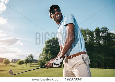 Smiling African American Man In Cap And Sunglasses Holding Club And Playing Golf