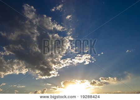 Vibrant sunset with sunbeams across blue sky with scattered white clouds