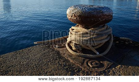 Rusty iron mooring bollard of a harbour with boat ropes.