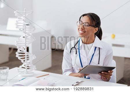 Modern genetics. Positive nice experienced scientist sitting at the table and looking at the gene model while doing a research