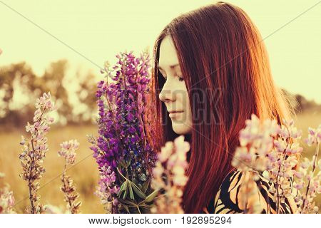 Happy red-haired woman with a bouquet of wildflowers. Village