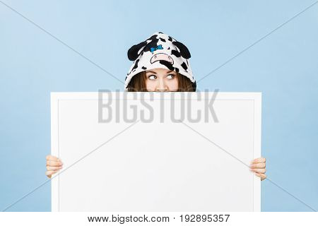 Teenage girl in funny nightclothes pajamas cartoon style covering her face with blank empty banner board. Advertisement copyspace.