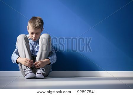 Depressed boy sitting on a floor in blue room