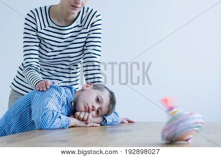 Sad boy and his mom looking at spinning top on wooden table