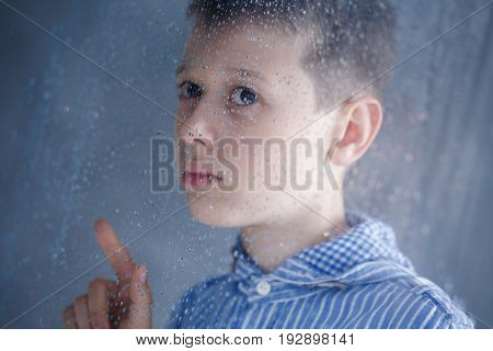 Sad boy behind the window on a rainy day