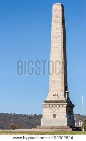 Hobart Australia - March 19. 2017: Tasmania. Closeup of tall light gray stone Cenotaph war memorial and tree on green hill under blue sky. Gulf War Iraq Afghanistan side. People.