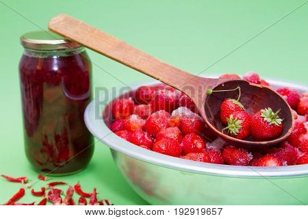 Strawberries from the manufacturer with sugar and jars for making jam on a green background.
