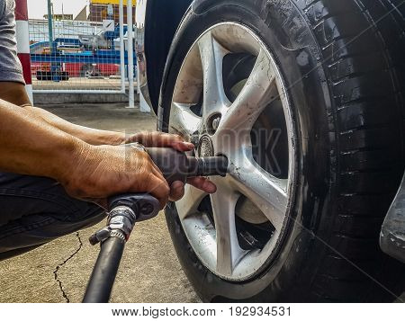 asian man hands holding pneumatic wrench screwing wet car tire for replacement after fixing air leak at garage.
