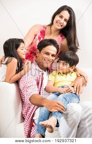 Candid Portrait of smart indian family of four while sitting on sofa. Indian or asian family group photo. Selective focus
