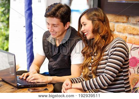 Smiling happy couple at the bar spending time together, while they are working in his computer.