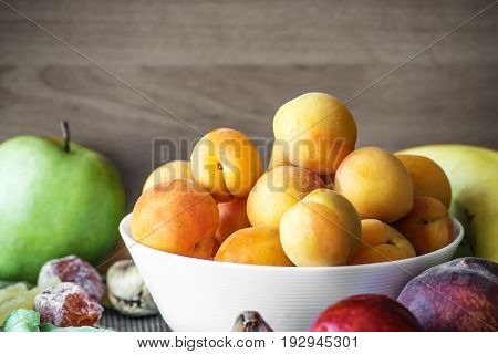 Fresh apricots in a white dish and other fruits on the kitchen table.