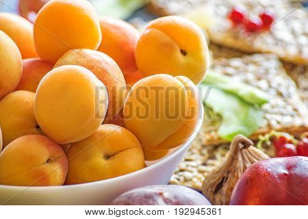 Fresh apricots in a white dish and other fruits on the kitchen table.