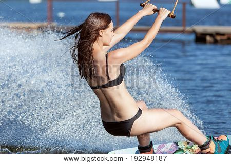 Woman in a bathing suit skates on the lake on wakeboarding.
