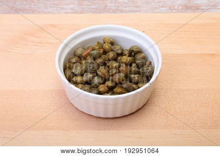 bowl with fresh capers on wooden table.