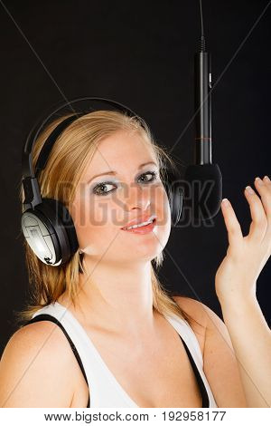 Music passion stage-fright concept. Blonde young woman singing to microphone and wearing big headphones on her head performing songs in studio.