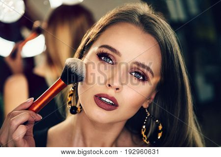 Beautiful woman doing evening makeup and holding makeup brush.