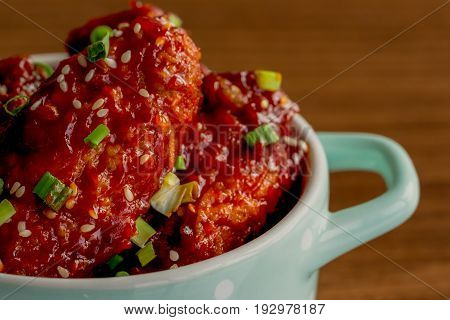 Korean fried chicken wings sprinkled with sesame and spring-onion on wood plate. Korean barbecue chicken wing delicious moist and spicy. Close up on fried chicken wings in Korean style on wood table.