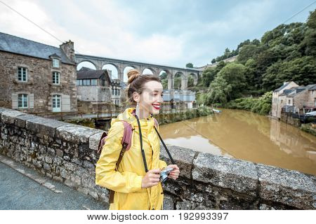 Young woman in yellow raincoat traveling with backpack and photo camera in Dinan village at Brittany region in France