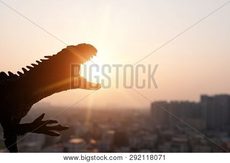 Silhouette Of Carnotaurus And Buildings In Sunset Time