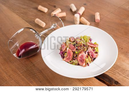 Duck Breast Salad With Glass Of Red Wine, Served On A White Plate, Decorated With Corks.
