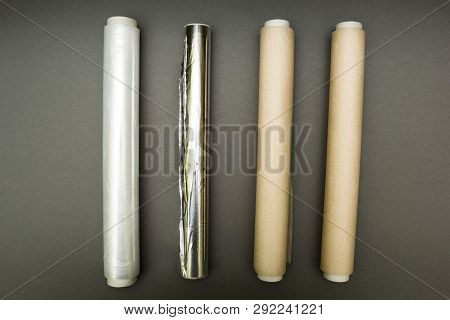 Plastic Wrap, Aluminum Foil And Roll Of Parchment Paper On Grey Background.