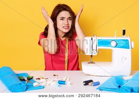 Close Up Image Of Unhappy Young Brunette Woman, Sits With Unpleasent Facial Expresions Near Broken S