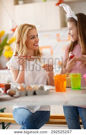 Cheeerful woman with girl coloring Easter eggs 