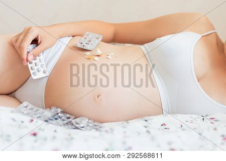 Pregnant Woman In White Underwear Lying In Bed With Many Pills. Young Woman Expecting A Baby And Hav
