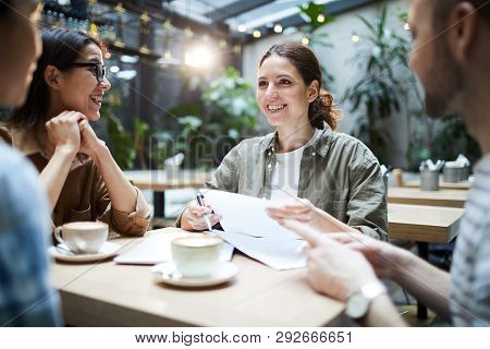 Cheerful Excited Young Startuppers Sitting At Table In Coffee Shop And Sharing Ideas And Strategies 