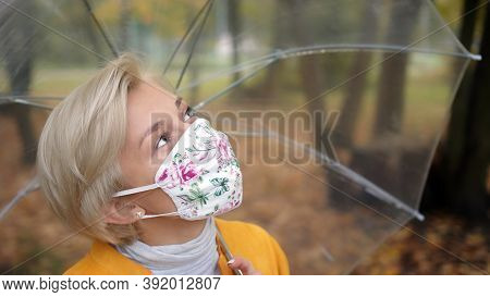 Beautiful Blond Woman With Face Mask Holding Transparent Umbrela In The Park In Autumn. Coronavirus 