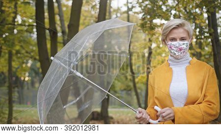 Young Caucasian Fashionable Woman With Face Mask Spinning Transparent Umbrela In The Park In Autumn.