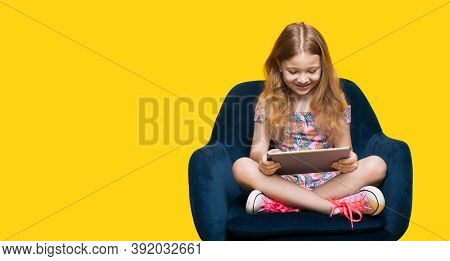 Blonde Caucasian Girl Is Playing With A Tablet Sitting In An Armchair On A Yellow Wall With Free Spa