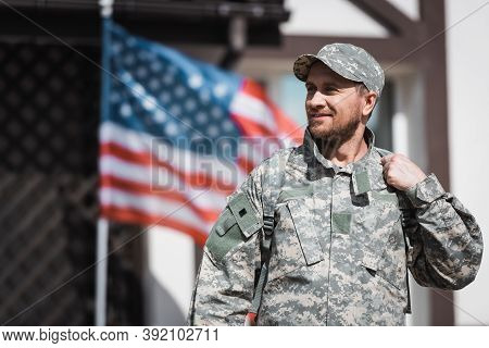 Military Veteran In Camouflage Looking Away With Blurred American Flag On Background