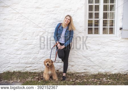 Labradoodle Dog And Woman Outside Close To A White Wall Brick