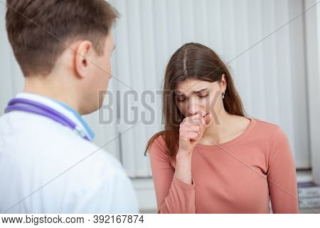Young Sick Woman Visiting Doctor At The Hospital. Female Patient Coughing While Talking To Her Docto