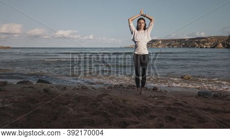 Young Caucasian Brunette Woman Doing Youga On The Sandy Beach In The Morning. High Quality Photo